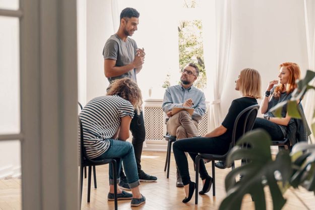 Happy hispanic man talking to his support group about his succes therapy group meets at PHP rehab